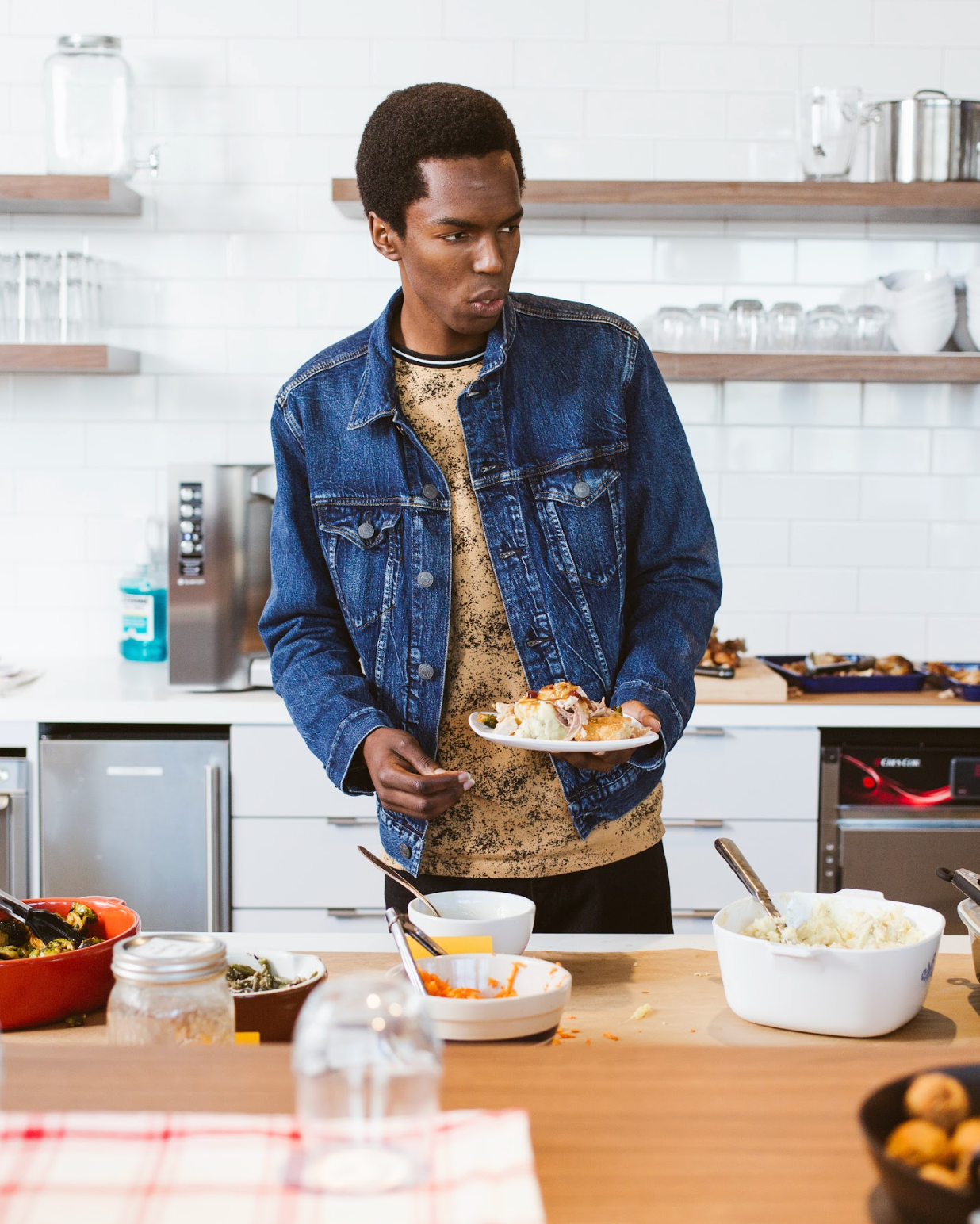 Person standing in a kitchen with various dishes and utensils on the counter.