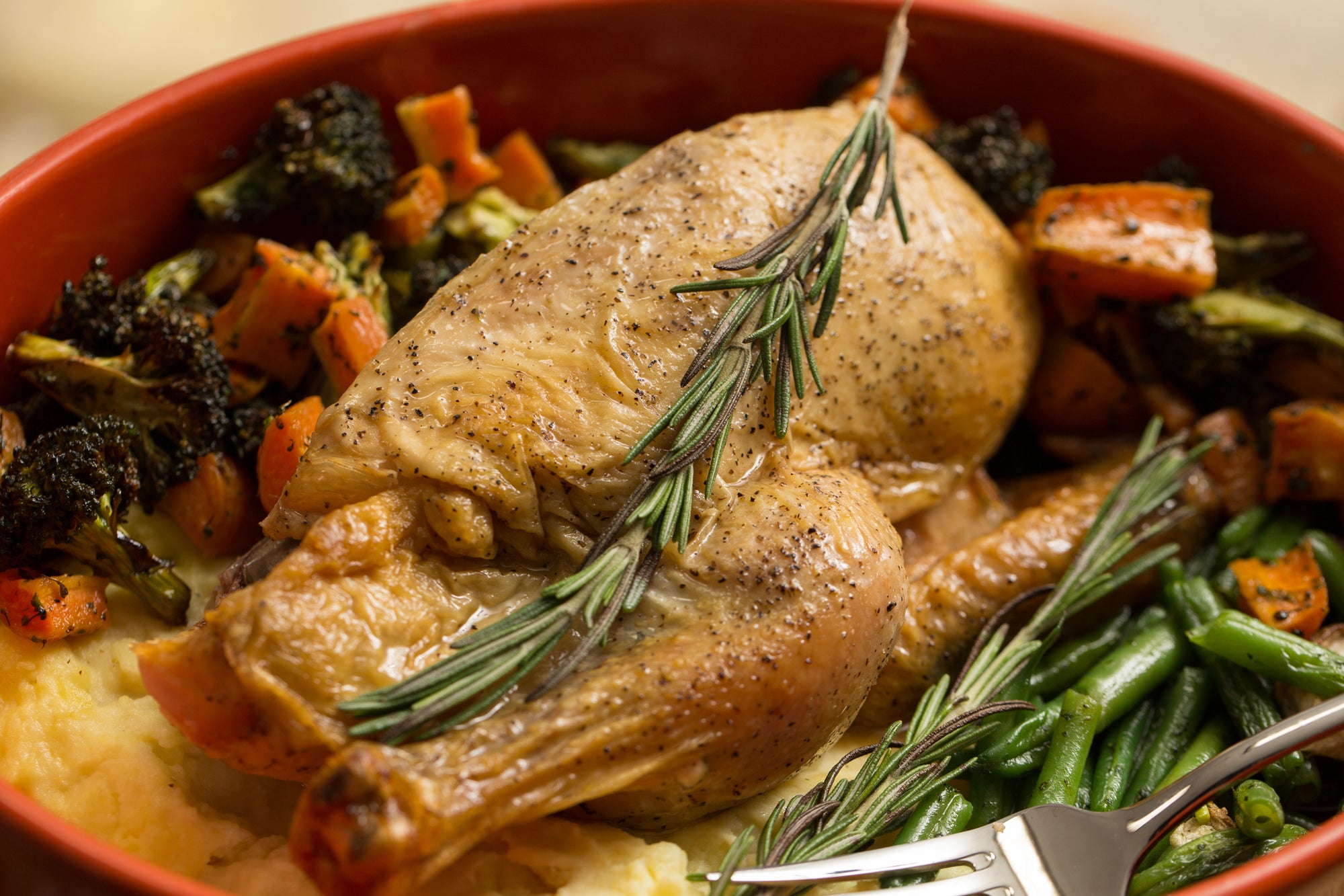 Rotisserie chicken in a bowl with roasted carrots, broccoli, and string beans.