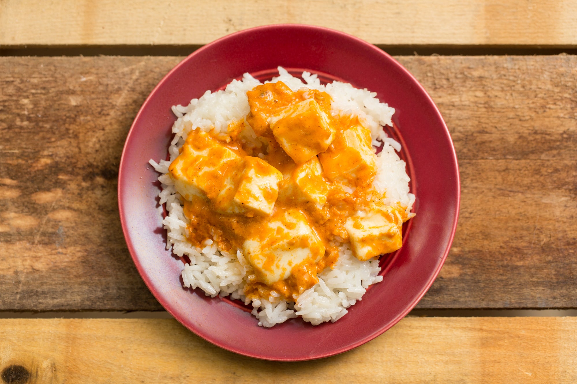 Paneer Tikka Masala on a bed of white rice, on a red plate.